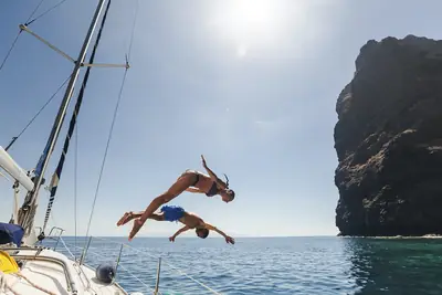 Two guests diving from a sailing yacht into the sea beside a rocky coast, Tenerife