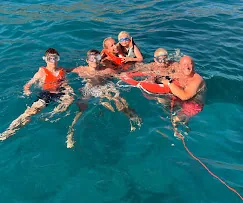 Freundesgruppe schwimmt mit Schwimmwesten neben der Yacht