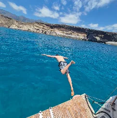 Guest diving off the yacht into clear blue water, south Tenerife coast behind