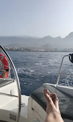 Pieds nus d’un passager dans le cockpit d’un voilier, côte de Tenerife au loin